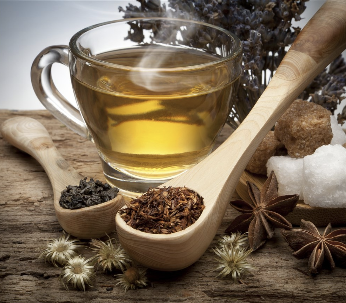 شاي يانسون دافئ في كوب شفاف زجاجي على طاولة خشب و ملاعق خشبية مملؤة باليانسون المجفف بجانب الكوب