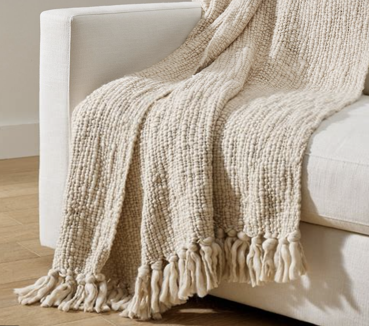 بطانية محبوكة بنسيج سميك (basketweave) بلون كريمي مع شرّابات، تعطي عمقًا وملمسًا غنيًا بدون نقش واضح