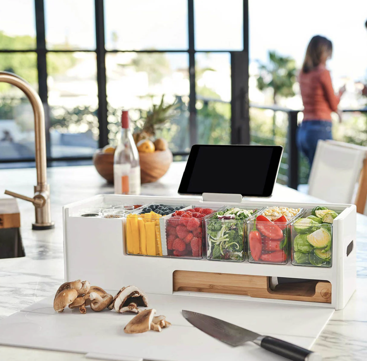 سطح تحضير مرتب قرب الحوض: لوح تقطيع وسكين أمام أدوات تحضير وخضار جاهزة، لتجهيز المكونات بسرعة.